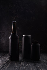 bottle and black metallic cans of beer on wooden table
