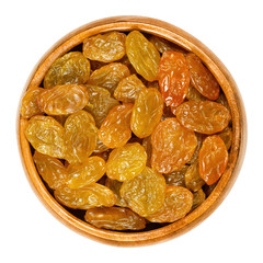 Sultanas, golden raisins, in wooden bowl. Big, golden-colored, dried grapes are eaten raw or used in cooking and baking. Close up, from above. Isolated macro food photo.