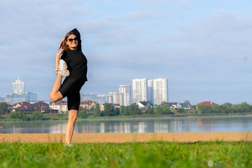 women stretching in the park near lake. city scape on background. morning exercises. young caucasian girl doing yoga, Natarajasana, standing in Lord of the Dance pose. fitness and healthy lifestyle.