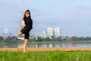 women stretching in the park near lake. city scape on background. morning exercises. young caucasian girl doing yoga, Natarajasana, standing in Lord of the Dance pose. fitness and healthy lifestyle.