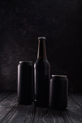 bottle between black metallic cans of beer on wooden table