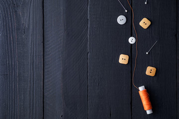 Orange spool of thread, pins and buttons for sewing on a wooden black background. Copy space