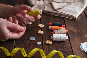 Fototapeta na wymiar Sewing kit for needlework on wooden background. Spool of thread in the hands of a seamstress