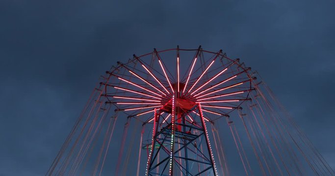 Amusement park red chain carousel with neon lights spinning around