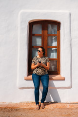 Portrait of beautiful young woman wearing animal print shirt and sunglasses using her mobile phone close to a wood window. Communication concept.