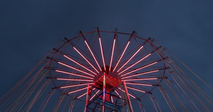 Amusement park red chain carousel with neon lights spinning around