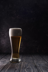 glass of fresh light beer with foam on wooden table
