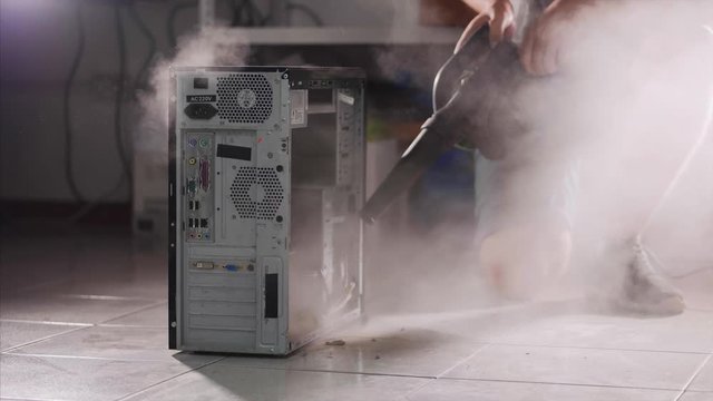 A man with a vacuum cleaner in hand is cleaning the computer at prophylaxis. A lot of dust is flying around the system unit in slow motion. Prevention service concept.
