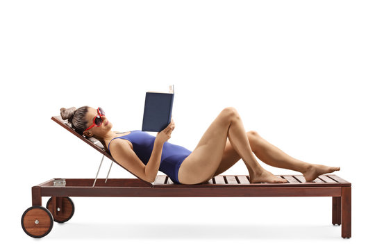 Young female in a swimsuit lying on a lounge chair and readng a book