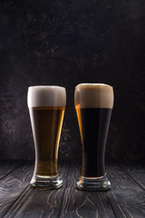 glasses of light and dark beer with foam on wooden table