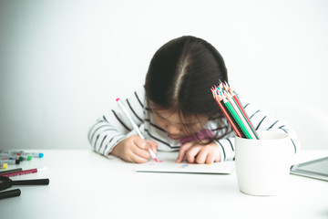 Blurred images of A 6 year old Asian girl are concentrating on making card for mothers on important occasions On white background, concept to children and education. This picture focuses on pencils