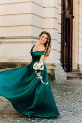 Pretty girl in an emerald dress posing on the background of the house