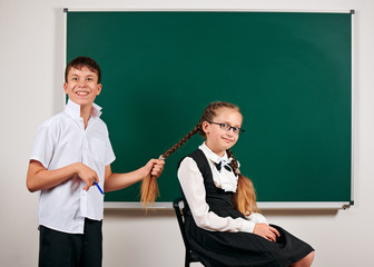 Portrait of a schoolboy and schoolgirl playing near blackboard background - back to school and education concept