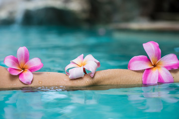 hands over the pool with flowers. Tropical flowers frangipani plumeria, Leelawadee floating in the water. The spa pool. Peace and tranquility. Spa concept.