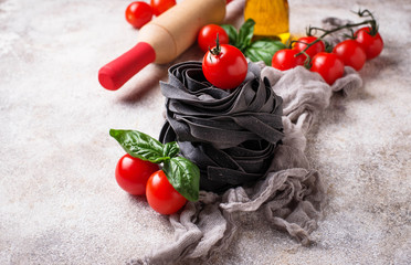Fototapeta na wymiar Black uncooked pasta with tomato and basil