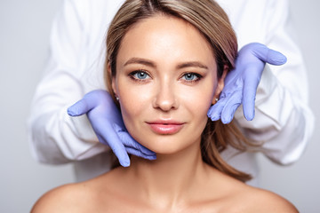 Close up portrait of young blonde woman with cosmetologyst hands in a gloves. Preparation for operation or procedure. Perfect skin, spa and care - obrazy, fototapety, plakaty