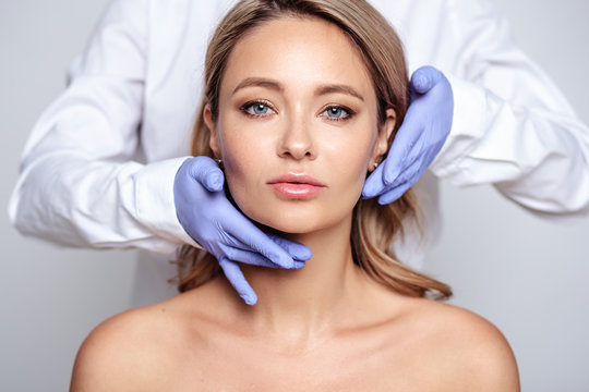 Close up portrait of young blonde woman with cosmetologyst hands in a gloves. Preparation for operation or procedure. Perfect skin, spa and care