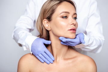 Close up portrait of young blonde woman with cosmetologyst hands in a gloves. Preparation for operation or procedure. Perfect skin, spa and care
