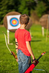 Rear view of a boy standing in front of an archery target before shooting