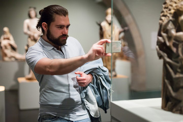 Adult male visitor using phone in sculptures exposition at museum