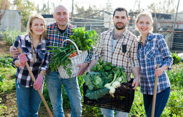 Family of four professional gardeners holding  harvest of vegetables and greens