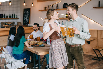 cheerful man and woman in traditional german costumes holding mugs of beer
