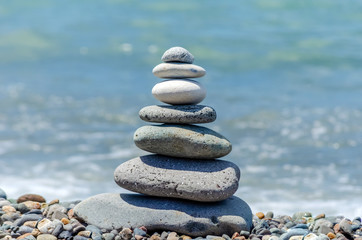 pyramid of sea pebbles on the beach against the backdrop of the sea wave in sunny day. concept of balance harmony and meditation. copy space