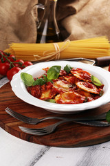 Ravioli with tomato sauce garnished with parmesan cheese and basil on rustic table