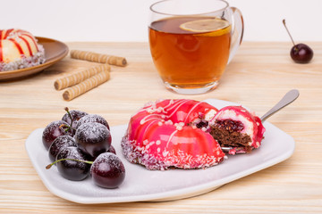 Elegant striped sponge cake with a shiny glaze, coconut flakes and sugar pearls in the shape of a doughnut. Piece on a fork, tea mug, wafer rolls