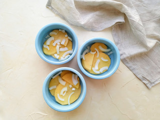 Fresh slices of potatoes and onions placed in round blue ceramic baking pans on a light background top view. Step-by-step preparation of casserole.