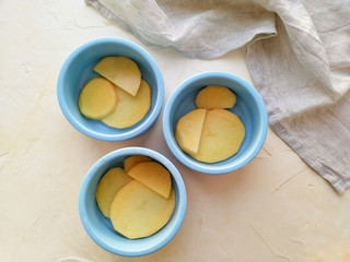 Potato slices in round ceramic baking pans of blue color on a light background top view. The process of cooking baked potatoes.