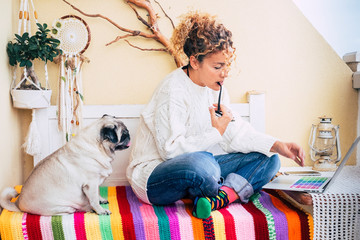 Alternative people at work beautiful adult woman at home outside in the terrace work with technology laptop computer and fat pug dog look at her sit down ona coloured trendy bench