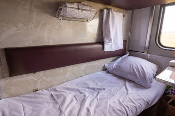 General view of the empty lower shelf of the reserved seat carriage of the train, spread bedding - obrazy, fototapety, plakaty