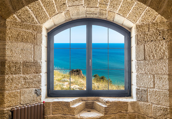 Fragment of a stone wall with a window. Seascape outside the window