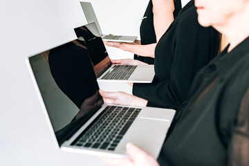 partial view of three-generation businesswomen in total black outfits holding laptops with blank screens isolated on grey
