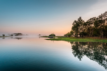 Sunrise at the Yellow Water Cruise, morning mist between trees and smooth water with mirror effect, Kakadu National Park, Northern Territory, Australia