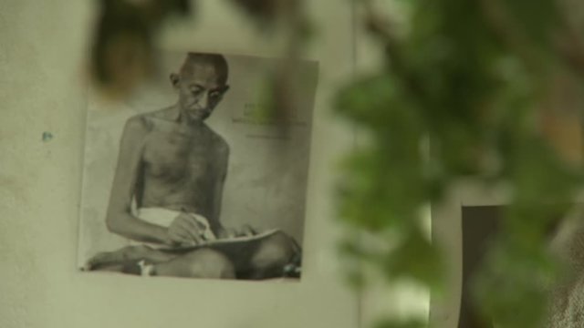 Steady, close up shot of tree leaves, the camera then focuses on a poster of Mahatma Gandhi on a wall.