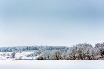 Winter landscape with trees by the river and forest in the distance_