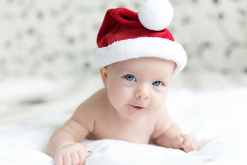 Little baby girl in red Santa hat cap smiling indoors on a bed with white background
