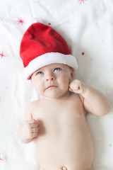 Little baby child girl laying on a bed with red stars and red hat of Santa on and thinking about gifts and Christmas