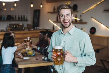 handsome young man holding mug of light beer and smiling at camera