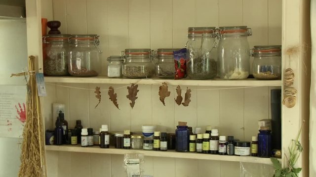 Steady, medium wide shot of a shelf containing bottles of oils and jars of herbs and spices.