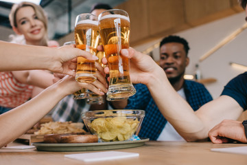 selective focus of multicultural friends clinking glasses of light beer in pub