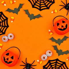 Halloween square frame of scattered candy and decor. Flat lay over an orange background with copy space.