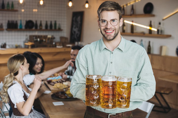 handsome young man holding mugs with beer and smiling at camera