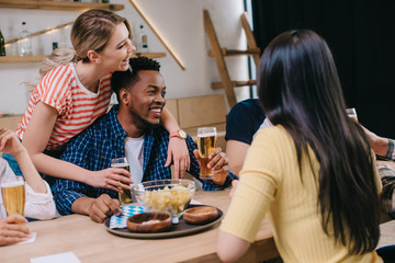 young woman hugging african american man near multicultural friends in pub