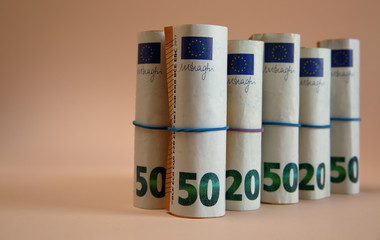Rolls of euro 50, 20 and euro tied with elastic blue and violet gum close up isolated on pastel apricot background