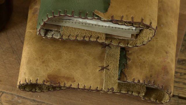 Steady, high angle, medium close up shot of leather bound binders container pieces of paper.