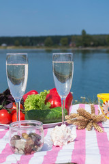 Beautiful picnic with fruits, vegetables and glasses of wine near lake. 