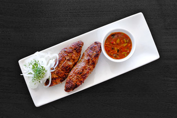 grilled kebab lamb meat food with vegetables and sauce on white plate on black wooden table background top down view of traditional turkish cuisine restaurant barbeque meal two pieces of roasted beef
